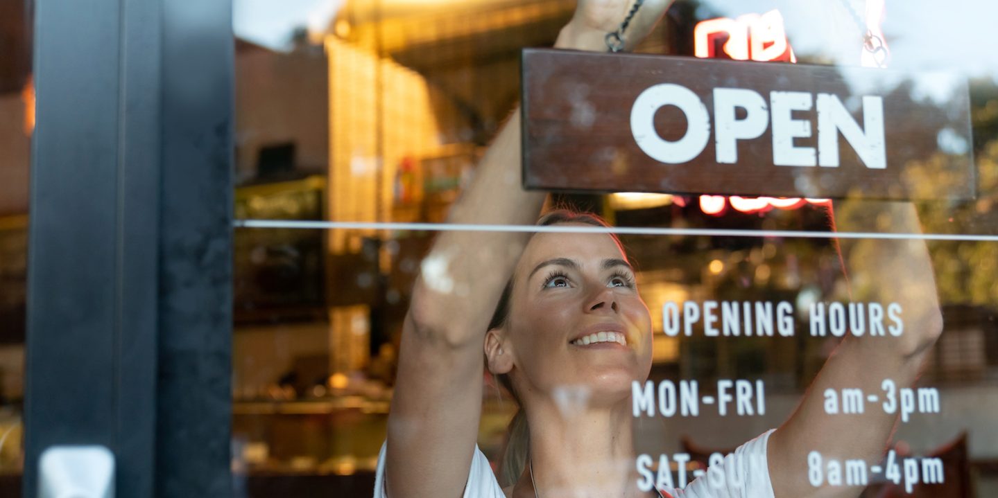Happy business owner hanging an open sign at a cafe